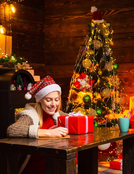 Woman is writing a christmas letter. New Year mood. Attractive woman in a Christmas room. Happy woman with Christmas gift over Christmas interior background.