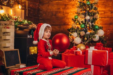 Noel ağacı için kocaman bir süs balosuyla küçük Noel Baba yardımcısı elf. Noel özellikleri. Mutlu ve parlak noeller. Noel Baba 'nın sihirli hediyeleriyle yardımcısı.