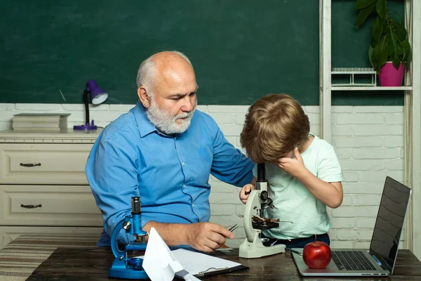 Přátelský chlapeček se starým dospělým učitelem ve třídě u tabule. Dědeček a batole se učí ve třídě. Vzdělávací proces. — Stock fotografie