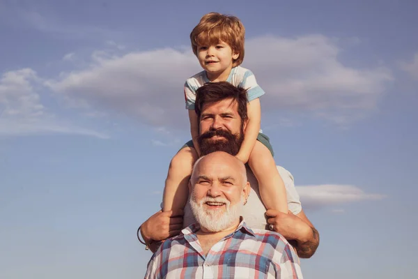 Babalar Günü. Büyükbaba, baba ve oğul kucaklaşıp birlikte eğleniyorlar. Mutlu çocuk yaz gökyüzü arka planında oynuyor. — Stok fotoğraf