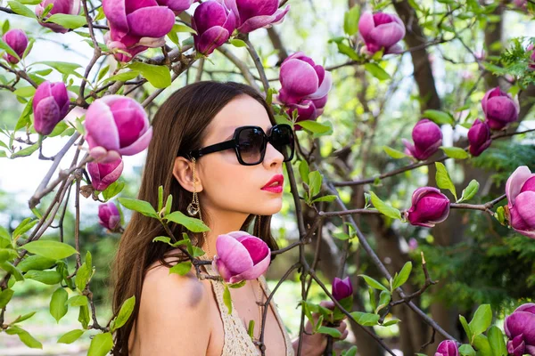 Foto de moda al aire libre de una hermosa mujer joven rodeada de flores. Retrato de una joven con gafas de sol. Hermosa joven en un jardín. Obra de arte de mujer romántica . — Foto de Stock