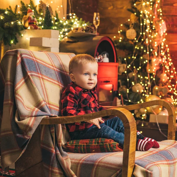 Kleines Baby, das im Stuhl auf dem weihnachtlichen Hintergrund sitzt. Frohe Weihnachten und frohe Feiertage. — Stockfoto