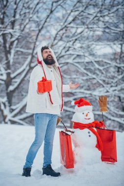 Kardan adam ve hediye getiren komik sakallı adam, arkadaşlar. Noel afişi. Kardan adam ve karda komik sakallı adam. Noel kış insanları portresi.