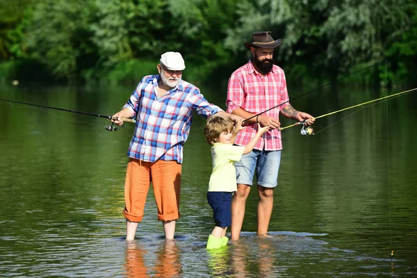 Nonno, padre e ragazzo pescano insieme. Un uomo che insegna ai bambini a pescare nel fiume. Felice giorno dei padri. 3 uomini che pescano sul fiume in estate . — Foto Stock