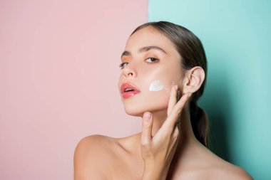 El kremi sürerek yanağa dokunan güzel genç bayanın portresi. Kişisel bakım rutini ve sağlıklı ruh hali. Saf pürüzsüz cilt ve doğal güzellik kavramı.