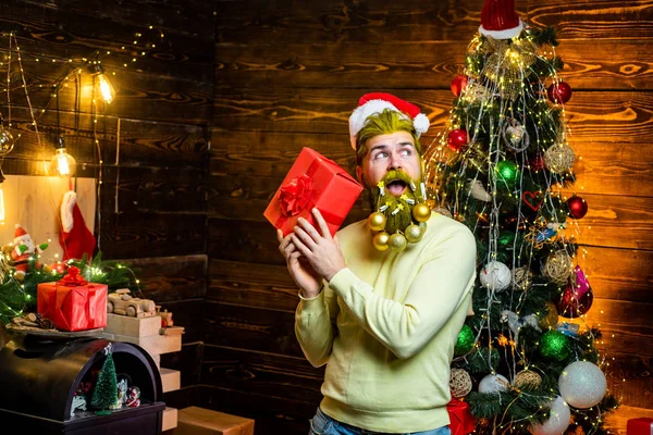 Santa Claus Hacer cara graciosa. Retrato de un guapo Santa hombre en el interior con regalo de Navidad. Papá Noel con barba blanca posando sobre el fondo de madera de Navidad. —  Fotos de Stock