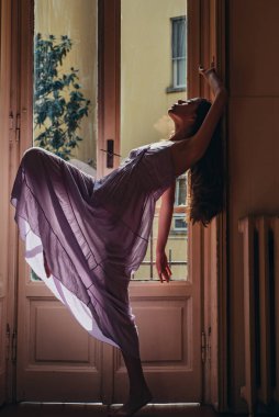 Kadın sabah balkonun yanında buluşuyor. Rahatlama zamanı. Pencerenin yanında duran genç bir kadın. Erotik gecelik. Tutku ve cazibe. Mutlu dans ediyor..