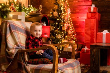 Tahta arka planda oturan mutlu, pozitif çocuk portresi ve lüks süslemeli odada Noel ağacı. Noel hediyeleri. Çocukluk anları.