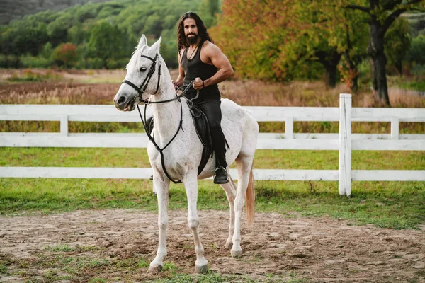 Cavalier sur cheval arabe gris dans le champ. Beau barbu qui monte à cheval à la ferme. Beau cheval avec cavalier homme trotter sur le terrain automnal. Concept d'amour équestre et animal. — Photo