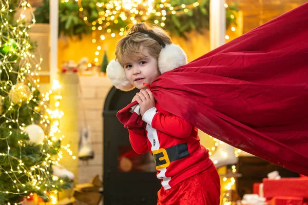 Filha do Pai Natal. Santa ajudante segurando um saco vermelho com presentes. Feliz Natal e feliz ano novo. Surpreendido Little Santa na sala de Natal. — Fotografia de Stock