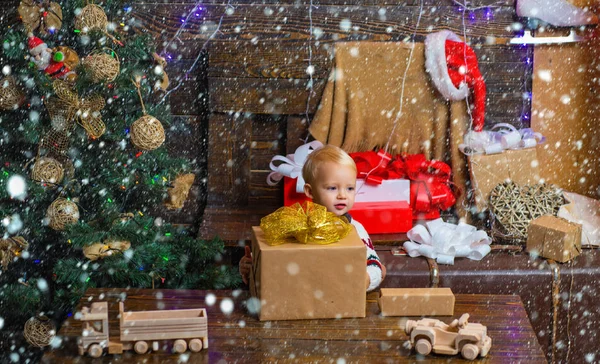 Férias de celebração. As crianças pequenas felizes no chapéu de Papai Noel com presente têm um Natal. Criança bonito alegre abrindo um presente de Natal. Um presente para as crianças. Noite de inverno em casa . — Fotografia de Stock