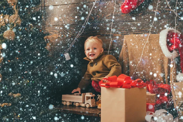 Niedliches kleines Mädchen schmückt den Weihnachtsbaum drinnen. Porträt Kind mit Geschenk auf Holzgrund. Neujahrskinder. Weihnachtsgeschichte. Glückliche Kinder. — Stockfoto