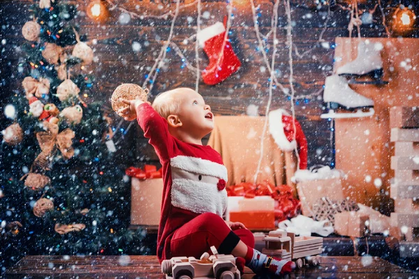 木製の背景にクリスマスと幸せな子。幸せなプレゼントとサンタ帽子で小さい子供がクリスマスを持っています。クリスマス冬の休日のコンセプトです。赤ちゃん. — ストック写真