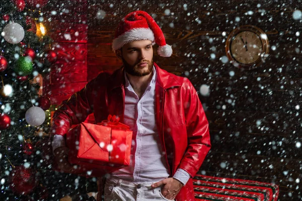 Christmas gifts. Man well groomed hipster in front of christmas decoration and new year background. Merry christmas and happy new year. Man fashionable stylish handsome santa with gift box surprise