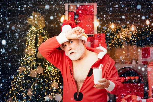 Fröhlicher Weihnachtsmann mit Glas mit Milch und Plätzchen mit Kamin und Weihnachtsbaum im Hintergrund. Frohe Weihnachten. — Stockfoto