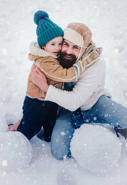 Táta a kluk se usmívají a objímají. Roztomilý syn objímá svého otce na zimní prázdniny. Vánoční pozadí. Venkovní portrét otce a syna v chladném slunečném zimním počasí v parku. — Stock fotografie