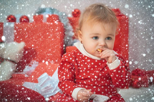 Kleine süße Baby-Puppe Mädchen, das Weihnachten Lebkuchen bei Neujahrsdiakorationen Hintergrund essen. kleines Mädchen im Weihnachtskostüm. Weihnachten. Neujahr. Heiligabend. Urlaub. Innenräume. — Stockfoto