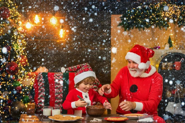 Pai e filho fazem um biscoito de Natal no fundo da casa de madeira. Ajudante de Pai Natal. Pequeno Papai Noel fazer biscoito para Papai Noel . — Fotografia de Stock