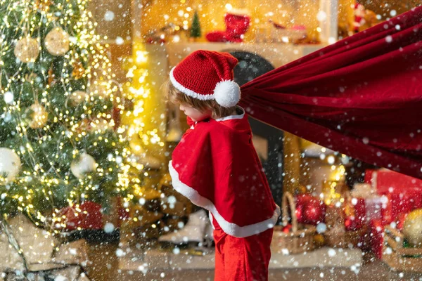 For Christmas and New Year posters. Funny little Santa Claus with huge red bag with presents. Santa child. Boy child play near christmas tree. Family holiday. — Stock Photo, Image