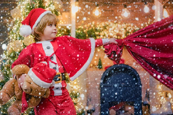 Sorprendió al pequeño Papá Noel en la habitación de Navidad. Niño adorable jugar Santa en casa. Niño Santa Claus con una bolsa llena de regalos. Funny pequeño Santa Claus con enorme bolsa roja con regalos . — Foto de Stock
