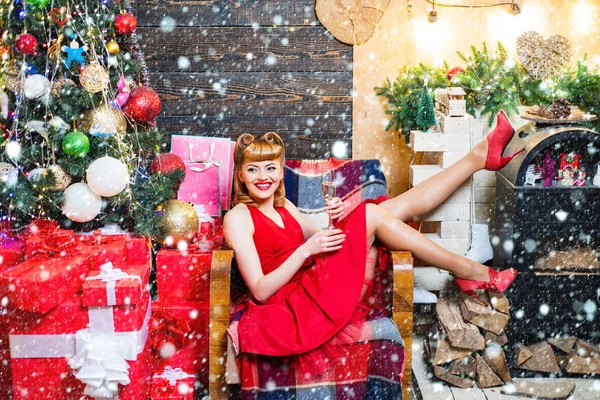 금발에 빨간 입술을 가진 아름다운 소녀가 선물 상자를 들고 있습니다. 전통적 인 크리스마스 트리 배경에서 포즈를 취하는 전통적 인 핀 업 여성. — 스톡 사진