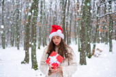 Vánoční dívka - sněhové efekty. Smějící se dívka venku. Venkovní portrét mladé krásné ženy v chladném slunečném zimním počasí v parku.