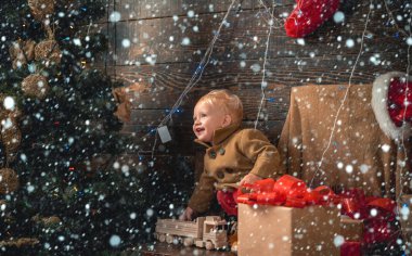 Karda Noel çocukları. Çocuk hediyesi. Noel kartı. Noel ağacının yanındaki oyuncak topuna bakan mutlu çocuk portresi. Noel Xmas kış tatili konsepti.