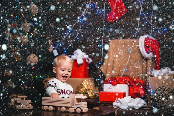 Crianças de Natal na neve. As crianças pequenas felizes no chapéu de Papai Noel com presente têm um Natal. Criança bonito está decorando a árvore de Natal dentro de casa. Noite de inverno em casa. Bebê alegre olhando para a câmera — Fotografia de Stock