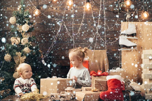 Weihnachtskinder im Schnee. glückliche kleine Kinder mit Weihnachtsmütze und Geschenk haben ein Weihnachtsfest. Winterabend zu Hause. Eröffnungsgeschenke zu Weihnachten und Neujahr. Frohe Weihnachten und ein gutes neues Jahr. Kinder — Stockfoto