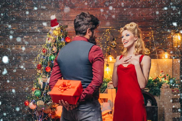 Hombre de Navidad en la nieve. Sorprendida, emocionada y feliz pareja navideña. Maquillaje y peinado de moda y belleza para Navidad. Belleza mujer rubia y hombre barbudo con regalo de Navidad rojo . —  Fotos de Stock