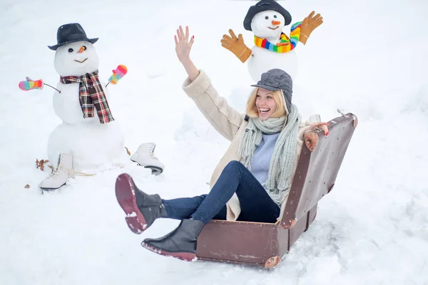 Happy smiling snow man and winter girl on sunny winter day. Winter holiday. Woman with suitcase. — Stock Photo, Image