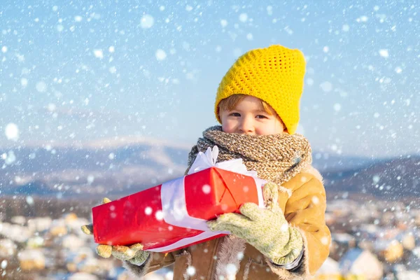 雪の中のクリスマスの子供たち。素敵な休日をお過ごしください。幸せな冬の子供は贈り物弓雪の背景を保持します。冬服の帽子とスカーフでかわいい男の子が閉じます。明けましておめでとうございます。 — ストック写真