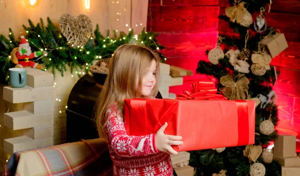 手に大きなクリスマスプレゼントを持つクリスマスの女の子。美しい女の子は赤いセーターを着て. — ストック写真
