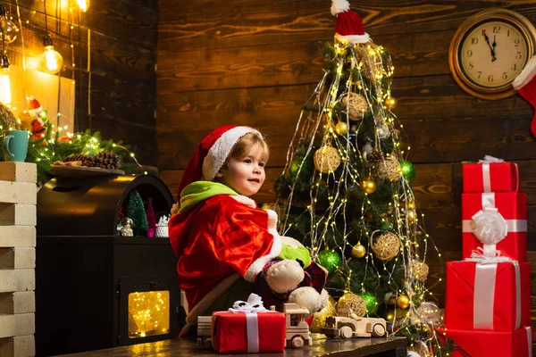 Criança feliz decorar árvore de Natal. Criança bonito feliz em chapéu de Papai Noel com presente ter um Natal. Conceito de Natal de Ano Novo. Criança se divertindo perto da árvore de Natal dentro de casa . — Fotografia de Stock