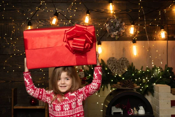 子供のためのクリスマスギフト-幸福の概念。手に大きなクリスマスプレゼントを持つ幸せなクリスマスの女の子。美しい女の子は赤いセーターを着て. — ストック写真