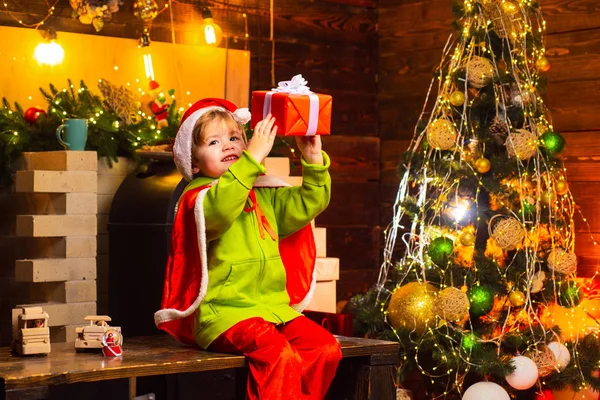 Zimní kluk. Vánoční děti. Dítě s darem. Zimní vánoční emoce. Dítě s vánočním dárkem na pozadí dřevěného domu. — Stock fotografie