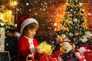 Karda Noel çocukları. Yeni yıl çelengi ışıkları. Noel zamanı. Mutlu küçük çocuk Noel süslemeleri ile oynuyor. Güzel bebek, Noel 'in tadını çıkar. Noel Baba küçük yardımcısı. Noel Baba 'nın Yardımcısı