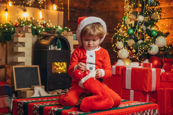 クリスマスプレゼントの靴下を着た幸せな小さな笑顔の男の子。新年のコンセプト。幸せな子供は贈り物を楽しんでいます。クリスマスツリーの背景. — ストック写真