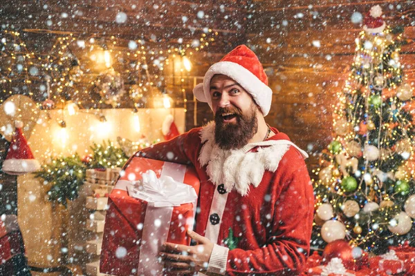 Vánoční muž ve sněhu. Santa muž držící dar. Hipster muž, vousatý Santa slaví Den díkůvzdání a Vánoce. Hipster v červené čepici Santa drží dárek. — Stock fotografie