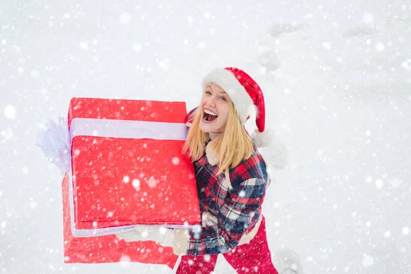 Femme dans la neige. Promotion et bonus. Joyeux Noël et Joyeuses Fêtes. Noël hiver gens. Fais un cadeau. Portrait de Santa femme avec un énorme cadeau rouge regardant la caméra . — Photo