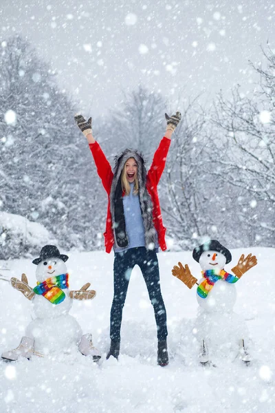 Mujer en la nieve. Muñeco de nieve divertido en sombrero elegante y bufanda con chica divertida en el campo de nieve. Chica feliz trenzado con un muñeco de nieve en un paseo de invierno nevado. Niña feliz muñeco de nieve y diversión de invierno . — Foto de Stock