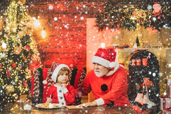 Família de Natal na neve. Criança escreve carta ao Pai Natal. Kid neto e avô em Santa Hat Writing Wish List - fundo luzes sem foco . — Fotografia de Stock