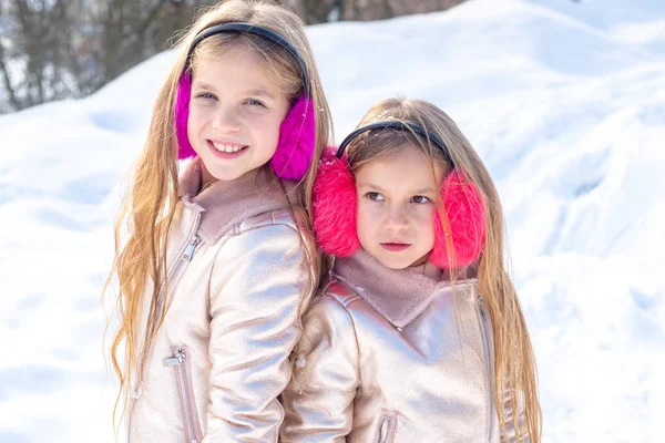Two little Girl playing with snow in park. Winter kids portrait. Two adorable young girls having fun together in beautiful winter park. Cute sisters playing in a snow. — Stock Photo, Image