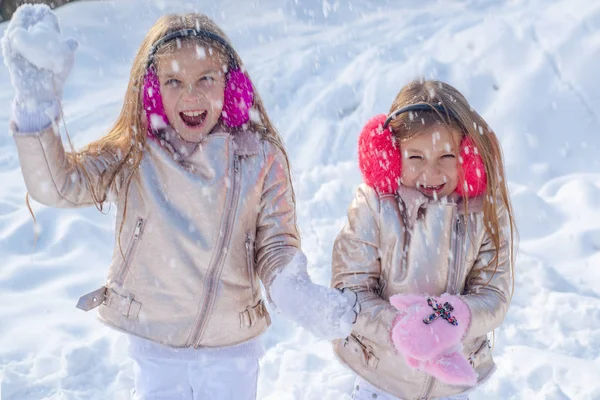 Les petites filles jettent des boules de neige dans le parc. Thème Noël vacances hiver nouvel an. Deux adorables jeunes filles s'amusent ensemble dans un magnifique parc d'hiver . — Photo