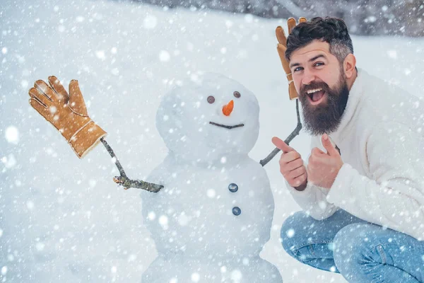 Christmas man in snow. Enjoying nature wintertime. Handsome bearded man, father in winter clothes. Christmas Man and snowman on white snow background.