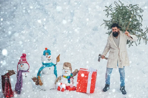 Christmas man in snow. Man with beard bears home a Christmas tree. Winter emotion. Merry Christmas and Happy Holidays. Young lumberjack bears fir tree in the white snow background.