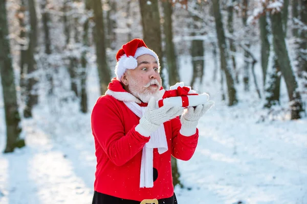 Le Père Noël souffle de la neige. Joyeux Père Noël soufflant sur la neige. Portrait du Père Noël heureux marchant dans la forêt enneigée et soufflant la neige magique de Noël. — Photo