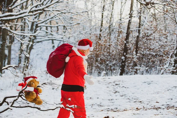 Santa nevoeiro mágico andando ao longo do campo. Papai Noel com saco andando no inverno. Dia de Acção de Graças e Natal. Real Papai Noel em boné vermelho puxando grande saco de presente vermelho . — Fotografia de Stock