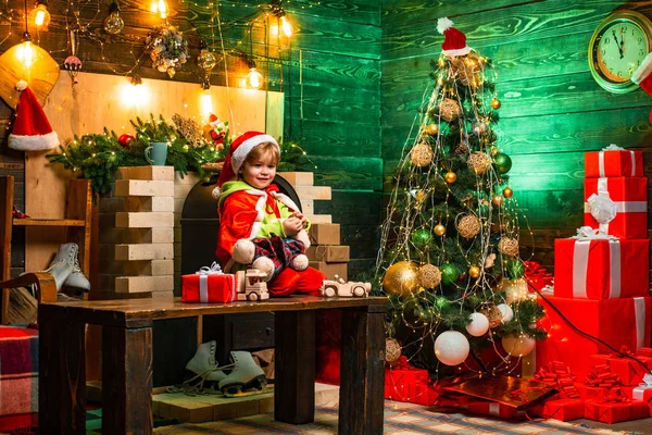 Año Nuevo. Niño con sombrero de Santa Claus y disfraz divirtiéndose. Descuentos de vacaciones. Niño pequeño decorando árbol de Navidad y regalos de apertura. Árbol de Navidad. Niño alegre cara tiene regalo en calcetín de Navidad. —  Fotos de Stock