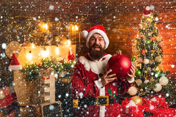 Hipster man, skäggiga Santa fira Thanksgiving Day och Christmas. Porträtt av Happy Santa med dekorativa Toy Balls nära julgran. — Stockfoto